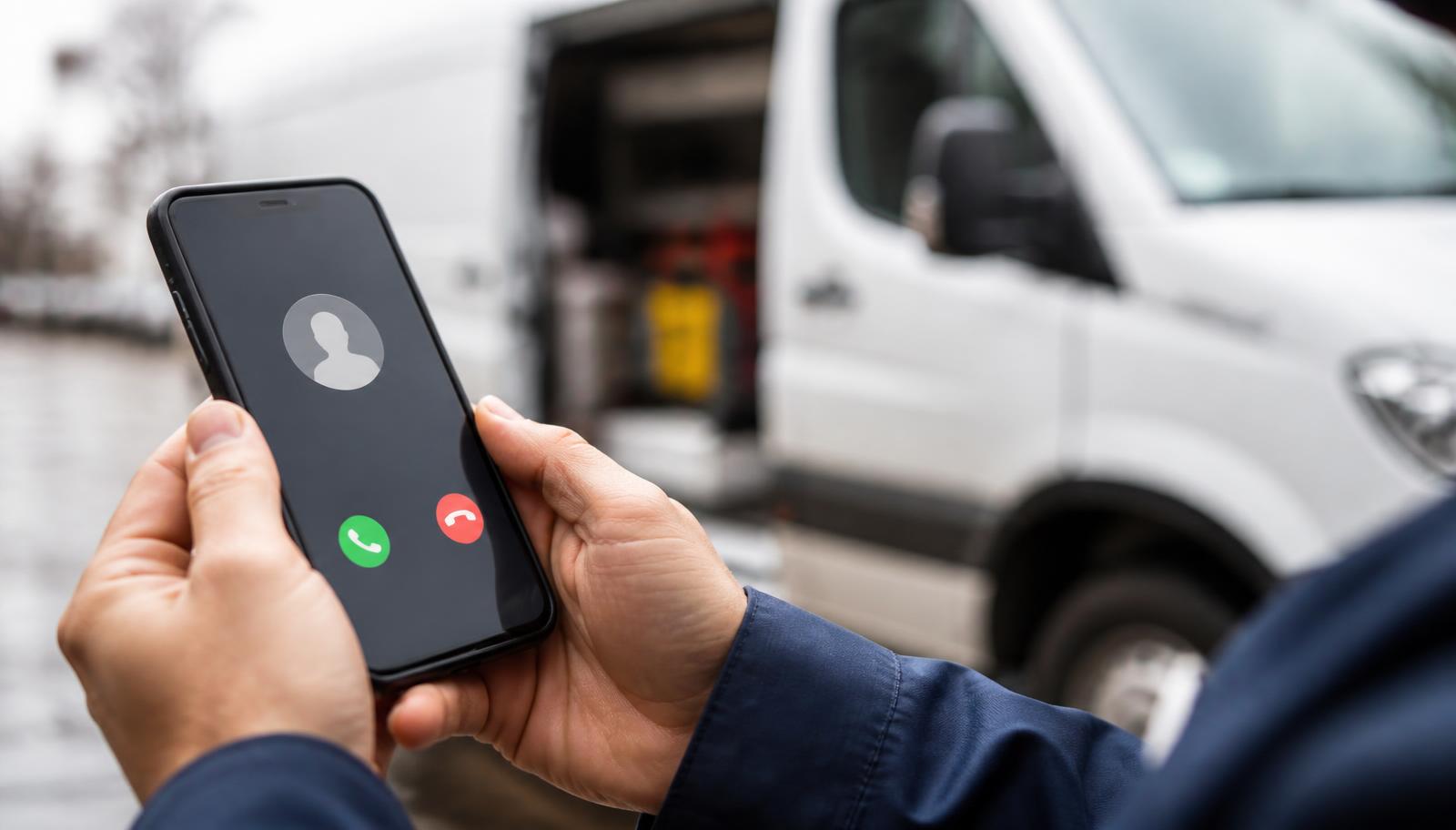 Technician answering an incoming call on a smartphone in front of a service van